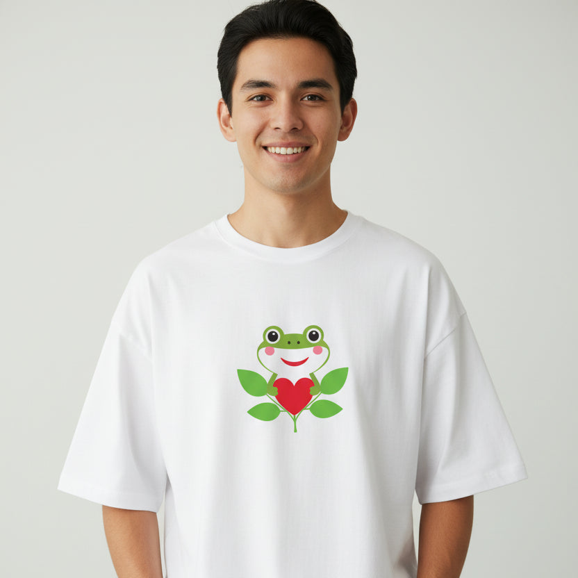 Person wearing a white t-shirt with a frog and heart design on a plain background
